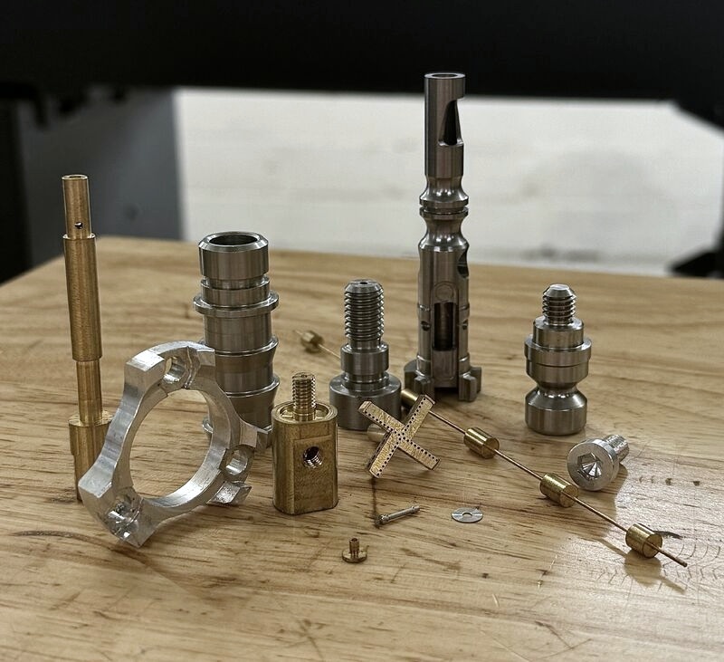 A selection of Piccolo machined parts including shafts, threaded components, miniature pins, and milled features